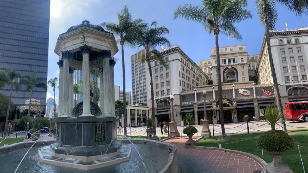 Columned fountain, palm trees, and historic buildings in a sunny urban plaza.