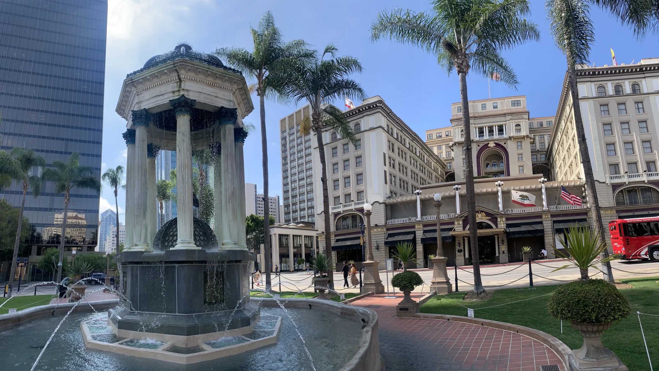 Columned fountain, palm trees, and historic buildings in a sunny urban plaza.